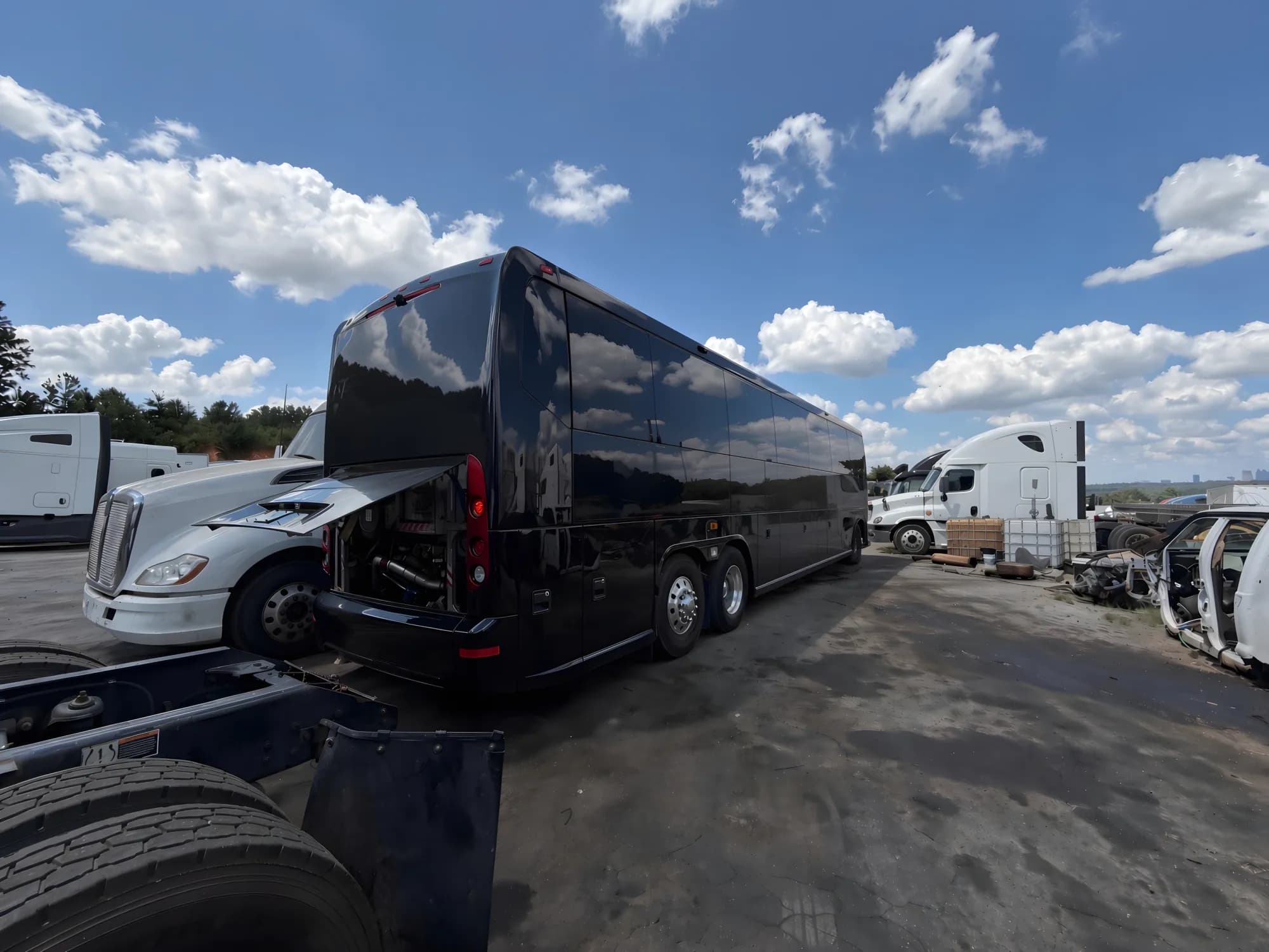 Motorcoach parked beside heavy trucks with its engine compartment accessible.